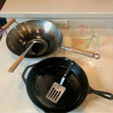 14-inch flat-bottomed carbon-steel wok next to 10-inch cast-iron skillet, pyrex measuring cup for hot oil
